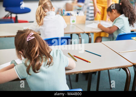 Lycéenne écrit au bureau de classe à l'école primaire leçon, vue arrière Banque D'Images