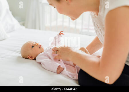 Jeune femme habiller fille bébé on bed Banque D'Images