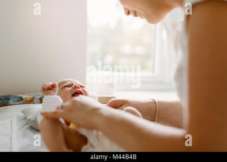 Jeune femme de changer la couche de bébé fille on bed Banque D'Images