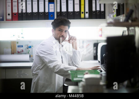 Portrait de jeune homme pharmacien à 24 using computer in pharmacy Banque D'Images