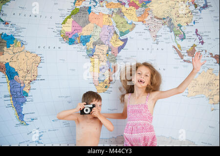 Petit garçon avec vintage camera girl dress s'amusant sur le fond de carte du monde Banque D'Images