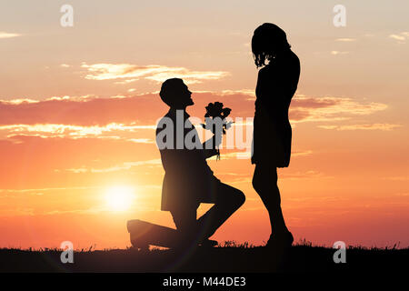 Silhouette d'un homme proposant sa petite amie contre ciel dramatique au coucher du soleil Banque D'Images