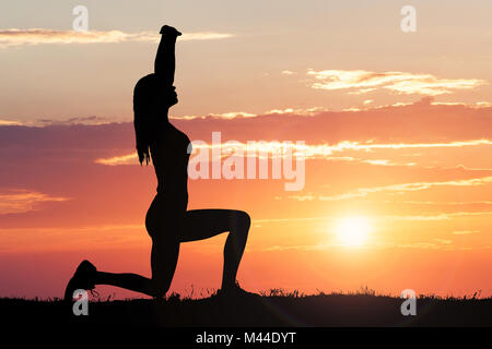 Silhouette d'une femme qui s'étend contre ciel dramatique au coucher du soleil Banque D'Images