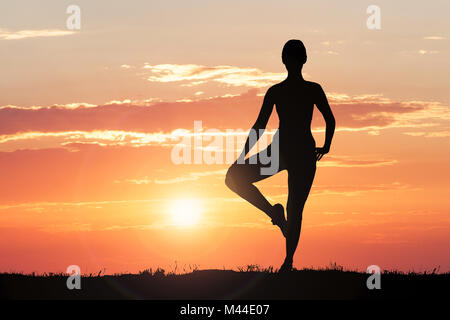 Silhouette d'une femme faisant de l'exercice dans le coucher du Soleil contre ciel dramatique Banque D'Images