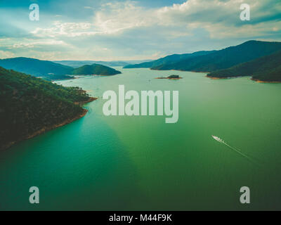 Vue aérienne de lonely bateau naviguant sur le magnifique lac au coucher du soleil au milieu des collines Banque D'Images