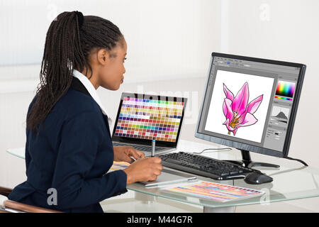 Designer femme fleur dessin sur ordinateur à l'aide de tablette graphique at desk in office Banque D'Images