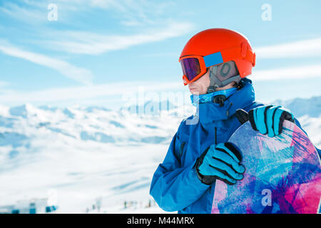 Photo de l'homme sportif casque en regardant ailleurs avec snowboard sur fond de colline de neige pendant la journée Banque D'Images