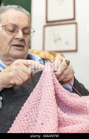 Femme âgée détendu au point sélective sur les mains accueil tricot laine rose gros plan Banque D'Images