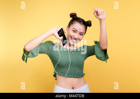 Fashion smiling asian woman listening to music in earphones sur fond jaune Banque D'Images