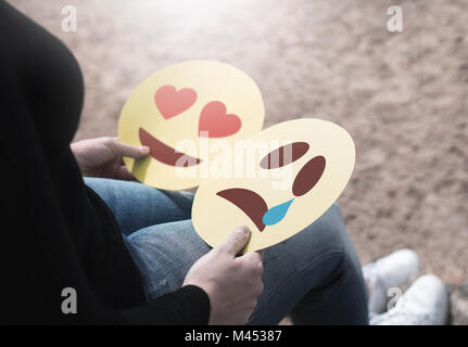 Woman holding 2 émoticônes en carton dans la main. Coeur d'amour et pleurer smileys. Le cœur brisé ou confus fille avoir des sentiments mitigés sur les émotions. Banque D'Images