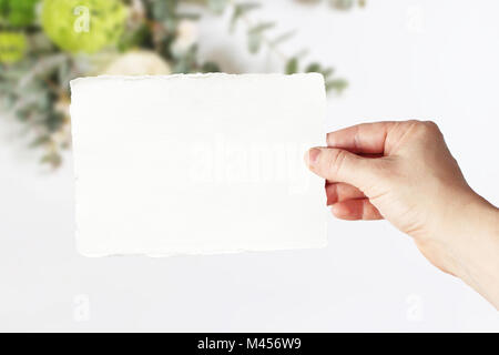 Stock photo style. Mariage féminin, maquette de carte de vœux d'anniversaire scène avec woman's hand holding en papier de l'espace carte. Floral background brouillée, em Banque D'Images