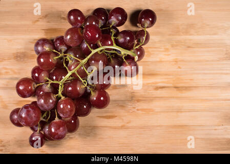 Les raisins rouges avec des tiges sur planche de bois rouge raisins frais d'arrière-plan. Banque D'Images