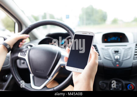 Jeune femme en chemise blanche à l'aide de smartphone pendant la conduite d'une voiture. Young Girl with cellphone volant Banque D'Images