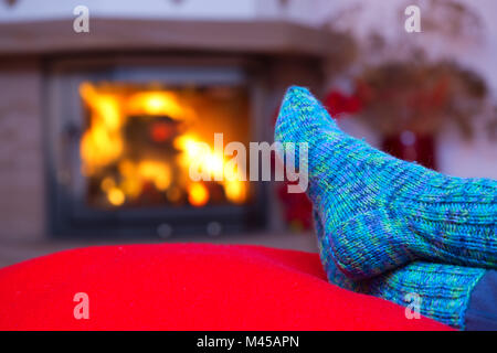 Pieds en chaussettes bleues de laine par la cheminée. Banque D'Images