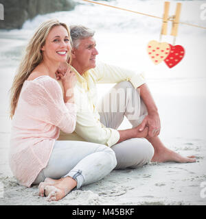Image composite de l'heureux couple assis sur le sable Banque D'Images