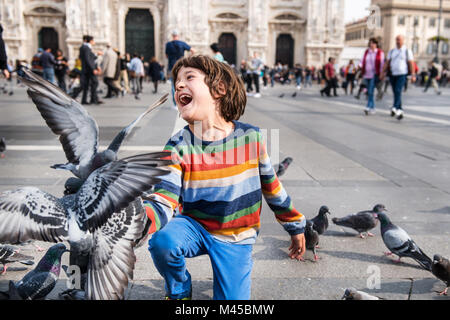 Garçon riant tout en alimentant les pigeons dans square, Milan, Lombardie, Italie Banque D'Images