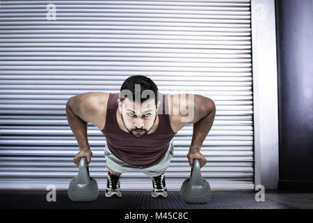Image composite de l'homme musclé faisant pousser ups avec kettlebells Banque D'Images