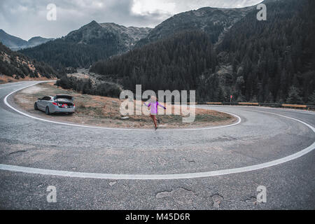 Jeune femme sautant sur route de montagne avec virage en épingle, Draja, Vaslui, Roumanie Banque D'Images