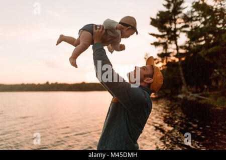 Man holding up baby daughter at lakeside Banque D'Images