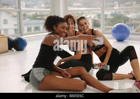 Smiling young girls prenant en selfies sport. Trois amies dans healthclub en tenant avec selfies téléphone intelligent. Banque D'Images