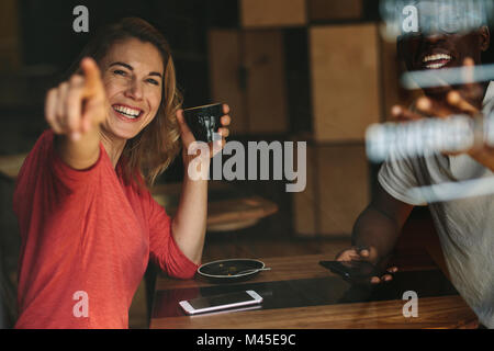 Femme souriante du doigt quelque chose assis à une table de café avec une tasse de café. Smiling woman sitting avec son ami dans un café. Banque D'Images