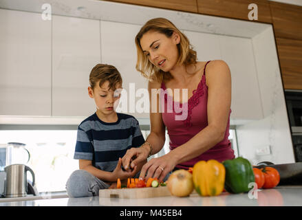 Mère fils aidant à couper des légumes frais dans la cuisine. Femme avec petit garçon à la cuisson des aliments à la maison. Banque D'Images