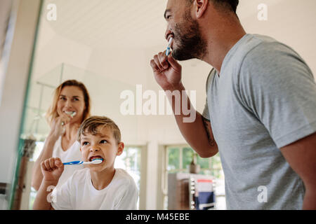Cute little boy se brosser les dents avec son père et sa mère dans la salle de bains. Jeune famille se brosser les dents ensemble dans une salle de bains privative. Banque D'Images