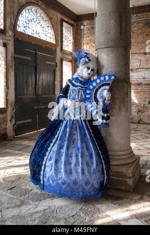Dame en masque peint et décoré de portefeuille, ventilateur en costume bleu orné robe, s'appuyant sur un vieux pilier au Carnaval de Venise Banque D'Images
