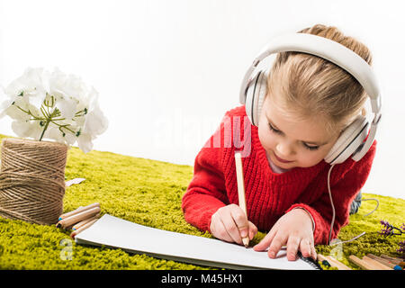 L'accent petit enfant dessin avec des crayons de couleurs et l'écoute de la musique sur tapis vert soft isolated on white Banque D'Images