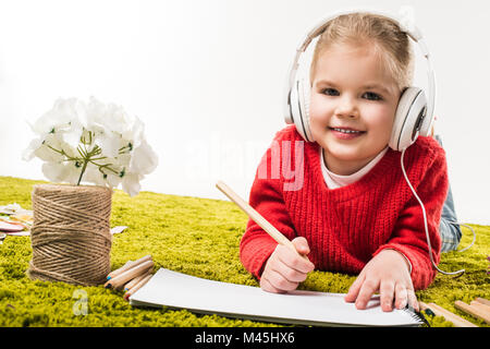 Heureux petit enfant dessin avec des crayons de couleurs et l'écoute de la musique sur tapis vert soft isolated on white Banque D'Images