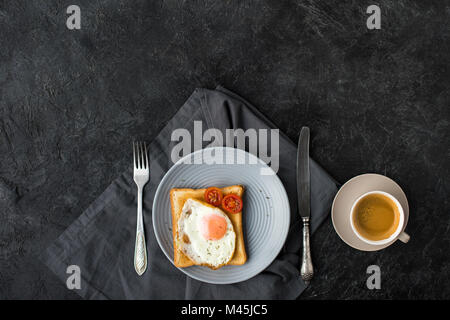 Mise à plat avec une tasse de café et des toasts avec des oeufs au plat et tomates cerises pour le petit déjeuner sur la surface sombre Banque D'Images