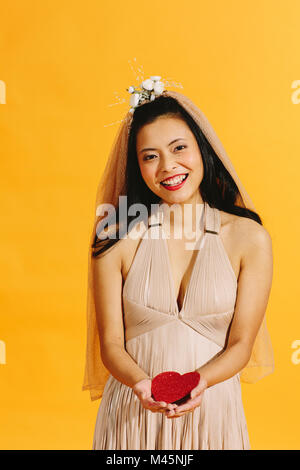 Smiling Asian bride holding a red heart looking at camera Banque D'Images