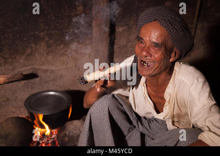 Homme qui fume le cigare birman local par le feu dans sa maison à Bagan Myanmar Banque D'Images