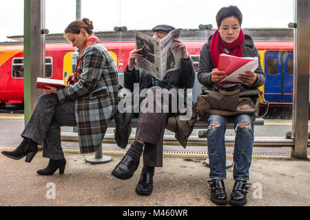 Trois étrangers assis sur un banc de la gare de la lecture d'un livre journal et notes au dossier Banque D'Images