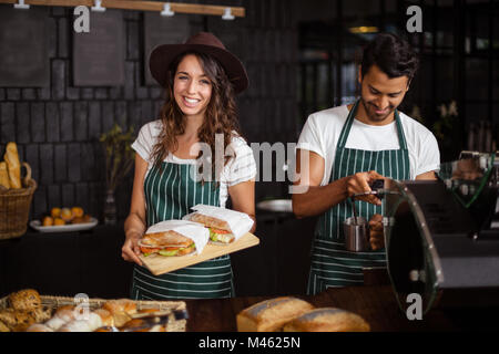 Baristas Smiling holding sandwiches et faire le café Banque D'Images