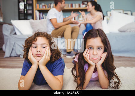 Frères et sœurs triste allongé sur tapis en parents assis en arrière-plan Banque D'Images