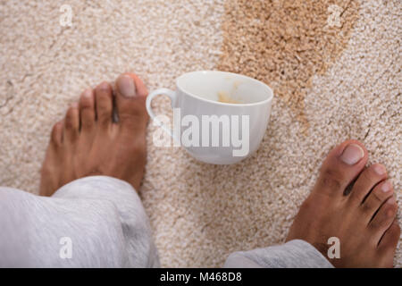 Close-up of a person's pieds debout près de café renversé sur la moquette Banque D'Images