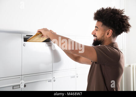 Vue latérale d'un jeune homme de mettre des lettres dans la boîte aux lettres Banque D'Images