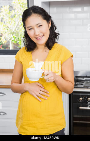 Smiling pregnant woman holding mug et toucher son ventre Banque D'Images