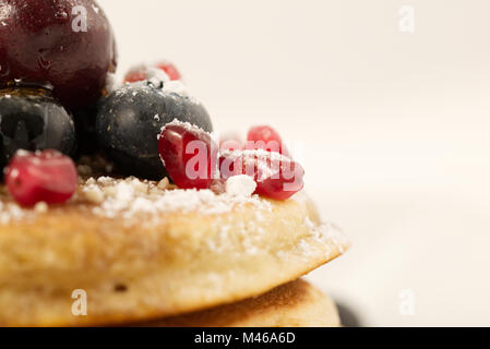 Petit-déjeuner de crêpes garnies de bleuets, cerises, graines de grenade et le sucre (sucre en poudre) et de sirop d'isolé sur fond blanc Banque D'Images