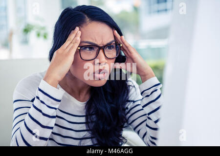 Fronçant Asian woman looking at laptop with hands on head Banque D'Images