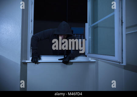 Entrer dans la chambre de cambrioleur à travers la fenêtre à la nuit Banque D'Images