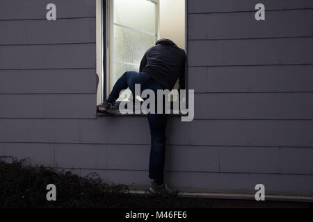 Vue arrière d'un cambrioleur d'entrer dans une maison par une fenêtre Banque D'Images