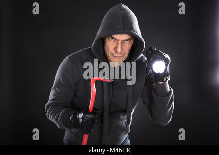 Portrait Of A Thief Holding lampe de poche et un pied-de-biche sur fond noir Banque D'Images