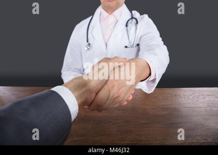 Close-up of a doctor Shaking Hand avec un patient de sexe masculin sur fond gris Banque D'Images