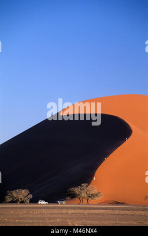 La Namibie. Désert du Namib. Sossusvlei. Numéro 45 des dunes de sable. Escalade touristes dune de sable. Devant les voitures 4x4. Banque D'Images