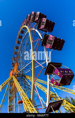 Vue depuis le bas vers le haut sur une grande, ronde, grande roue multicolore jaune avec supports et stands de framboise sur un fond bleu Banque D'Images