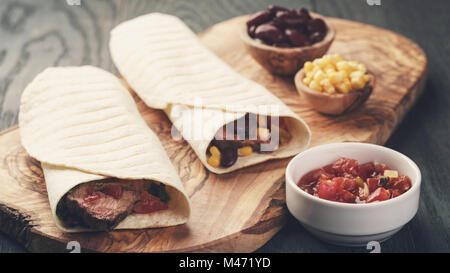 Burritos avec pavé de boeuf, le maïs, les haricots noirs et sauce salsa on cutting board Banque D'Images