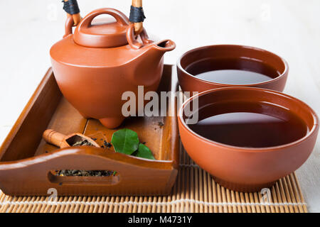 Théière en céramique et les feuilles de thé sur un plateau en bois thé Oriental. Banque D'Images