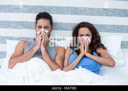 Jeune couple couvrant nez pendant l'éternuement on bed Banque D'Images